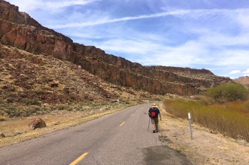 A solo traveler walking along a street inside a remote state park in Nevada, surrounded by rugged landscapes and grassy pathways.