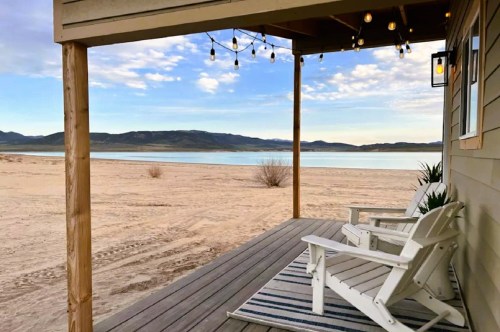 Views from a lakefront bungalow at a campground in Utah with a small furnished deck, a pretty lake, and mountains in the distance.