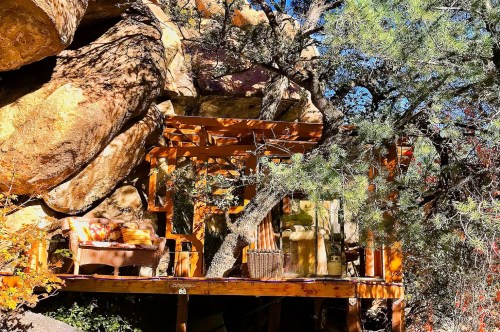 A treehouse Airbnb in Arizona nestled inside a rock cliff, with a furnished deck surrounded by towering trees.