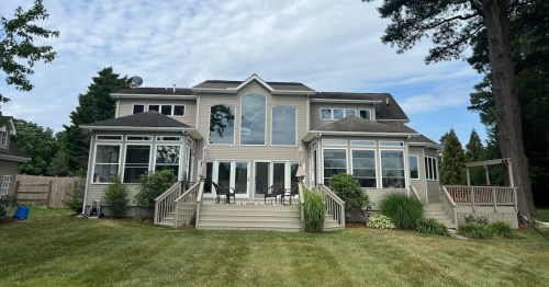 a photo of a two-story beige colored house with stairs and a deck and a mowed grassy lawn