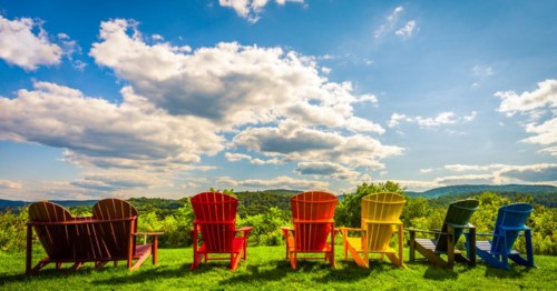 Six colorful Adirondack chairs sit in a line overlooking the mountains at the Sharon Welcome Center in Sharon, Vermont.