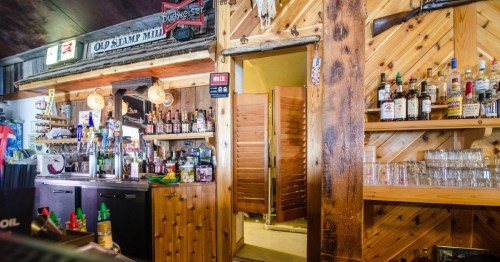 Warm wood interior of a restaurant bar area with shelves of various spirits and glasses; a wooden saloon door leads to the kitchen. Atlantic City, Wyoming