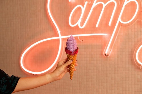 Hand holding a waffle ice cream cone with sprinkles on the rim with purple ube ice cream in it.