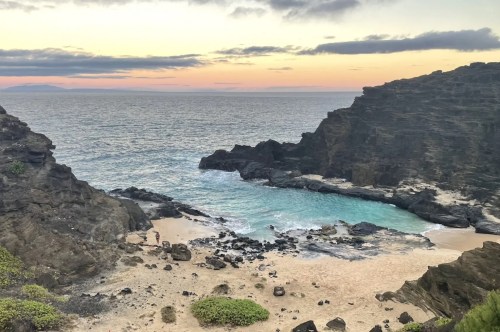 A small beach cove at dusk, with dark tall rocks surrounding it.