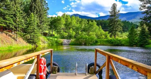 Views of a fishing pond with a small deck at an Airbnb in Colorado, surrounded by a wooded area with mountains in the distance.