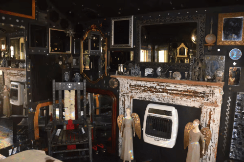 A living area within the Magical & Spooky Mirror House Airbnb rental in Warren, New Hampshire. The walls are decorated with multiple mirrors. An old fireplace and rocking chair are pictured.
