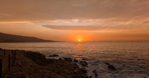The sunset over the Pacific Ocean colors the sky a bright pink.