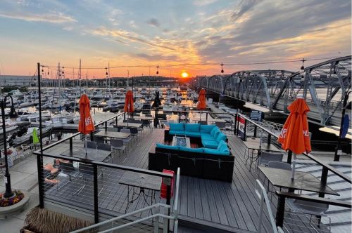 Waterfront patio dining with tables, a fire pit, and a couch.