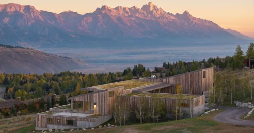 A large, luxury home Airbnb built into a hillside above Jackson, Wyoming. The Teton Mountains light up against a sunset sky.