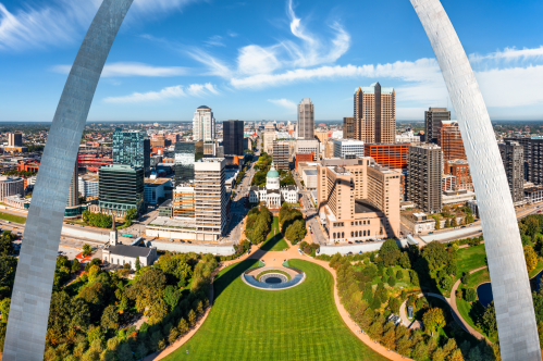 A view through the Gateway Arch shows the park below and the skyline of the city extending into the distance.