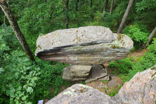 Ticklish Rock, a massive balanced boulder, viewed from above in a lush green forest, with a person partially visible below.