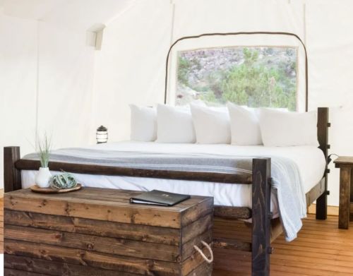 A bed and a wooden table in a luxury camping tent.