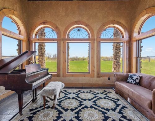 A piano room with a rug and a couch overlooking a vineyard..