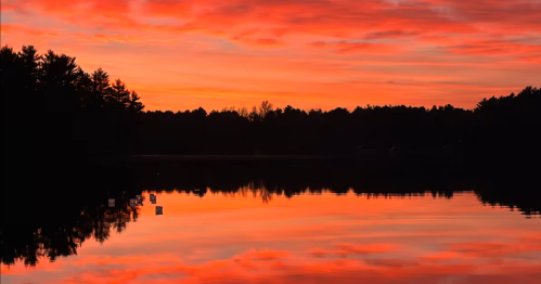 Orange and pink sunset sky reflect on a glassy lake as seen from a lakeside Airbnb in Wisconsin.