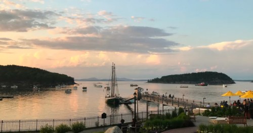 Sunset over Bar Harbor, Maine, with boats bobbing in the water and people enjoying the view along the shore.