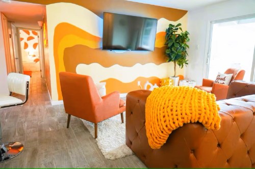 A cheery living room with retro vibes, featuring bright orange wallpaper and muted furniture inside a 70s-themed Airbnb in Phoenix.