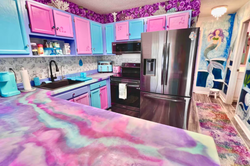 The kitchen at the Mermaid Den Airbnb rental in Ocean City, Maryland. It is decorated in bright pink, purple, and teal colors. The counter top is made of colorful epoxy.