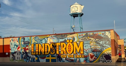 A colorful mural depicting Lindström, Minnesota sits beneath the town's coffee-pot shaped water tower.