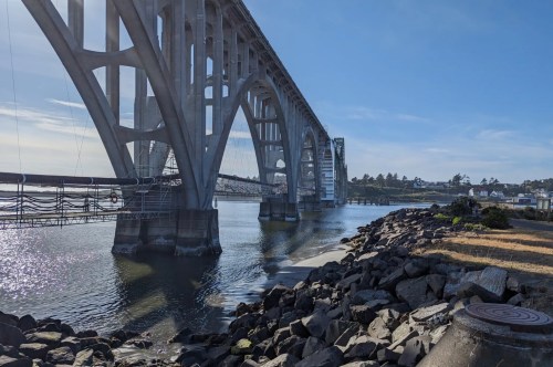 A large metal bridge towers over a river with a town and rocks on both sides.