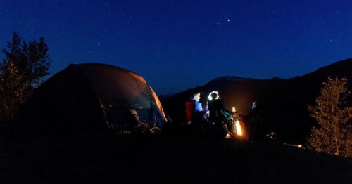 Views of a campsite featuring a tent and a family sitting around a campfire underneath a nighttime sky with twinkling stars.