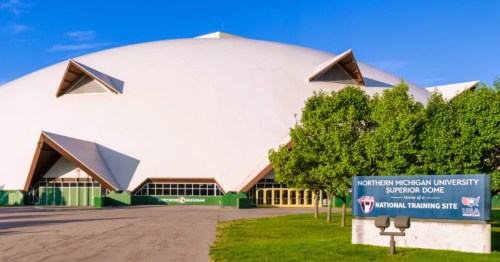 Large cream-colored dome, a popular roadside attraction in Marquette, Michigan, surrounded by trees, with a blue sign for Northern Michigan University