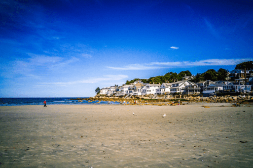 A view of Nahant beach in Nahant, Massachusetts. Several houses are in the background. A lone person is pictured in the distance.