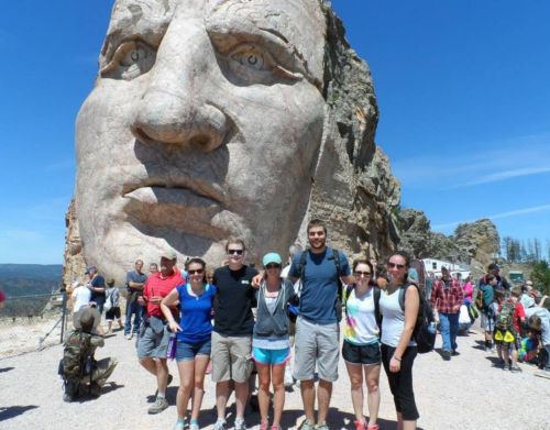 A group of young people standing in front of the face of the Crazy Horse Memorial.