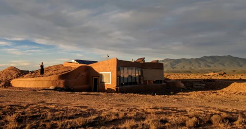 Modern + Mesa Taos Earthship in El Prado, NM, with sustainable adobe walls and solar panels under a vast sky.