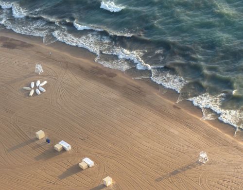 An aerial view of a beach with white structures on the sand.