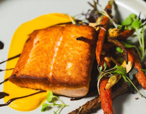 A close-up of a cooked fish with roasted carrots.