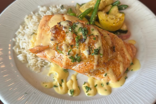 White plate with salmon filet and vegetables over rice