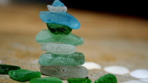 A vibrant collection of sea glass stacked together, showcasing shades of blue, green, and brown against a neutral background.