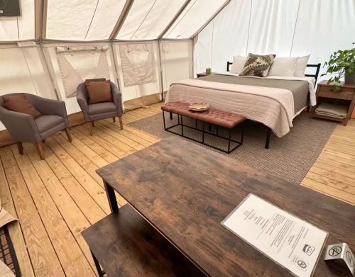 The inside of a canvas glamping tent with a bed, two chairs, and a wooden coffee table.