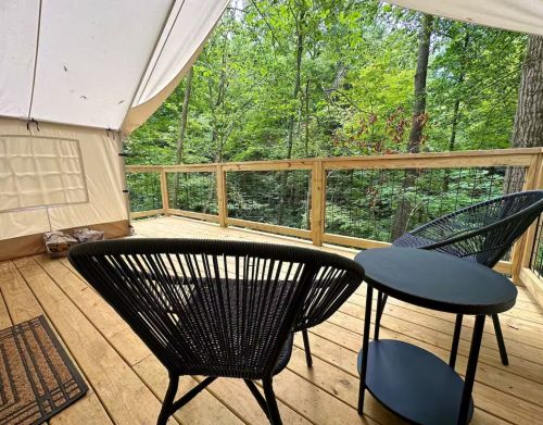 A wooden deck with patio chairs under a canvas tent roof.
