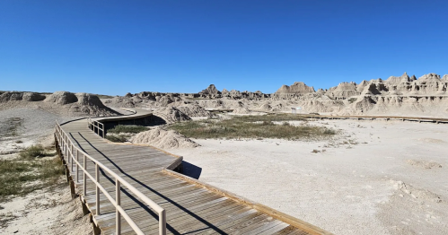 A curving boardwalk trail leads through a desolate landscape with rock formations at Badlands National Park, South Dakota.