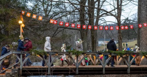 Festival-goers walk across a foot bridge under mini Swiss flags.