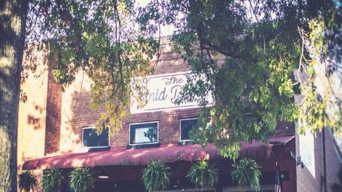 Trees frame the exterior of the Enid Diner in Mississippi with a red awning and brick facade.