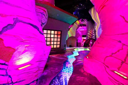 A neon pink interactive art exhibit with colorful designs and patterns in the background at Meow Wolf Omega Mart in Las Vegas