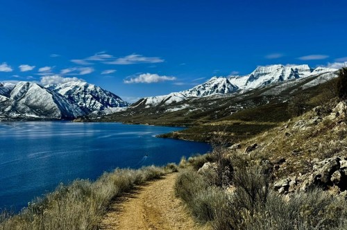 Views of a shimmering waterway inside a European-style waterfront village in Utah, surrounded by a walking trail and snow-capped mountains in the distance.