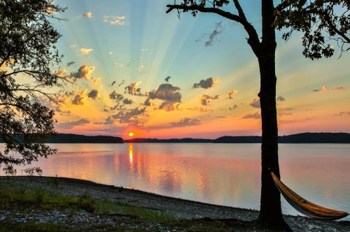 Views of a colorful sunrise reflecting on Lake Ouachita in Arkansas with a hammock hanging from a tree on the shores.