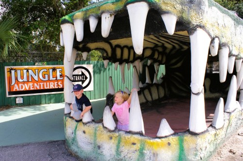 Views of Swampy, the world's largest alligator, featuring a massive gator head with large teeth, with a couple of kids laughing and posing for pics.
