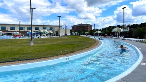 People sit in clear inner tubes and float down the clear water of a lazy river in a concrete channel at a municipal water park.