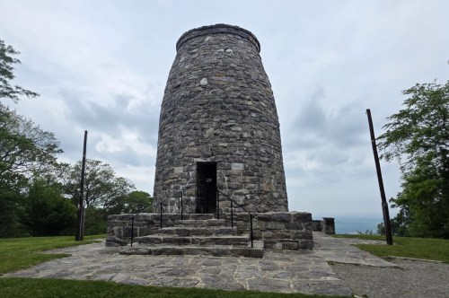 A tall, thin, stone monument sits in the middle of a green park on a cloudy day.