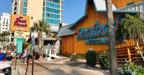 Exterior of The Back Porch Seafood and Oyster House in Destin, Florida, an orange building with a large Adirondack chair in front.