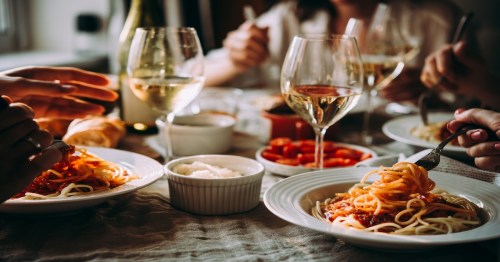 Friends having a pasta dinner with white plates and clear wine glasses.