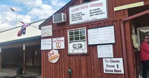 A red barn covered in menus and signs describing the food on offer, including barbecue and desserts.