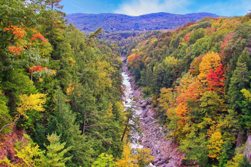 View of Quechee Gorge in autumn, with the stunning gorge bursting with fall colors. Mountains in the background.