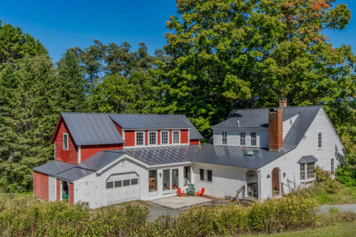 A modern barn-like home with red and white paint surrounded by lofty trees under a bright blue sky
