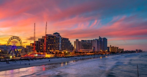 A colorful Daytona Beach sunset, featuring reflections on the water and attractions in the background.