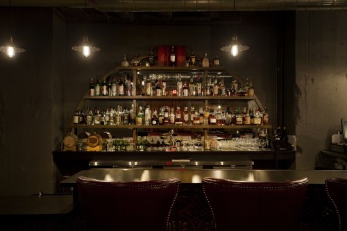 Liquor bottles on a bar shelf with candles in a dark room